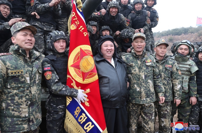 金正恩身穿黑色皮褸在一輛坦克前與一群軍人合照。